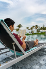 Rear view of Asian man reading book at swimming pool