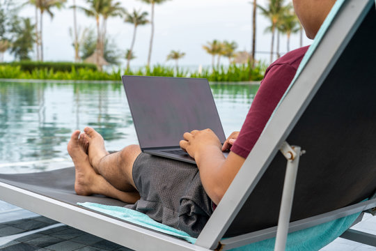 Asian man using laptop at the swimming pool - Powered by Adobe