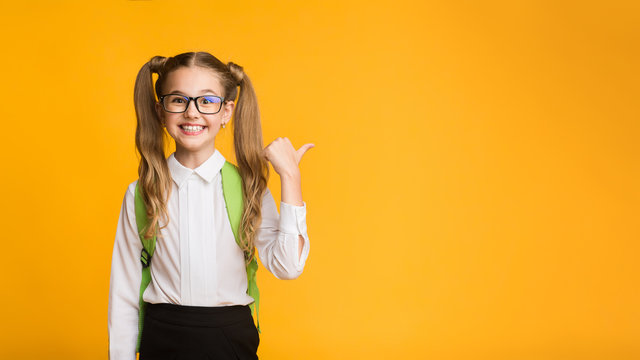 Cheerful Elementary School Girl Pointing Thumb At Copyspace On Yellow