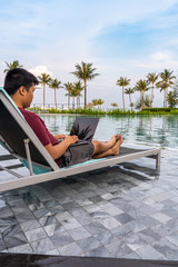 Man sitting at poolside chair and using laptop