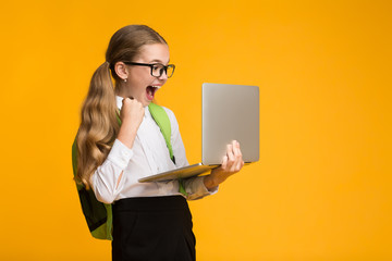 Excited Schoolgirl Playing Computer Games On Laptop Over Yellow Background