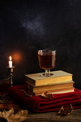 A cup of hot tea, books, a woolen knitted blanket, a candle, autumn leaves on a vintage wooden table. Autumn cozy mood. Low key. Copyspace. Vertical