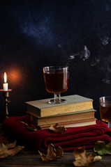 A cup of hot tea, books, a woolen knitted blanket, a candle, autumn leaves on a vintage wooden table. Autumn cozy mood. Low key. Copyspace. Vertical