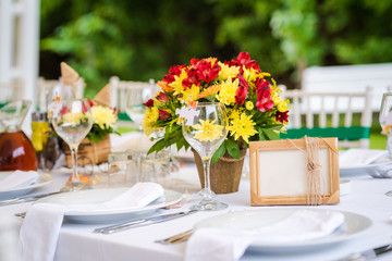 Fototapeta na wymiar Garden wedding table set up decoration - fresh red and yellow flowers and a blank photo frame/board