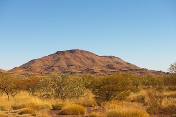 Panoramic view of mountain and bush vegetation of Pilbara outback landscape in Western Australia, with sunny blue sky as background.
