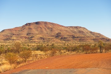 Panoramic view of mountain and bush vegetation of Pilbara outback landscape in Western Australia, with sunny blue sky as background.