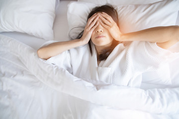 Woman stretching in bed after waking up, back view. Woman sitting near the big white window while stretching on bed after waking up with sunrise at morning, back view.