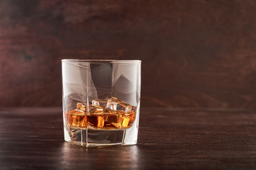 Glass of whiskey with ice on a wooden table