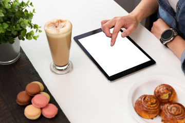Woman with smartwatch using tablet in coffee shop. Coffee and pastry, macaroons on white table. Freelance working