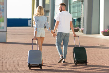 Fototapeta na wymiar Loving couple walking to airport entrance with luggage