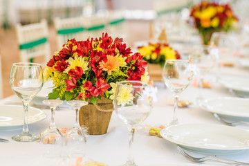 Fototapeta na wymiar Wedding table set up decoration made of red and yellow fresh flowers. Rustic/ garden wedding decoration