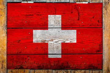 National flag of Switzerland on a wooden wall background.The concept of national pride and symbol of the country.Flag painted on a wooden fence with metal nails.