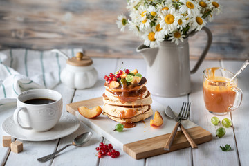 Cornmeal pancakes with salted caramel served with berries and fruits on a white wooden background.