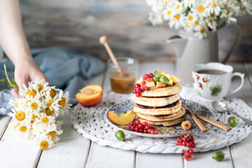 Obraz na płótnie Canvas Cornmeal pancakes with honey, served with berries and fruits on a white wooden background.