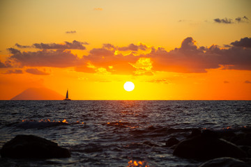 Sunset with sailboat in front of it, and stromboli