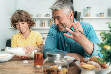 Happy boy making breakfast with milk, sitting near father