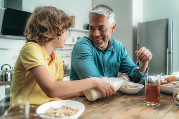 Kid making breakfast with milk, sitting near father