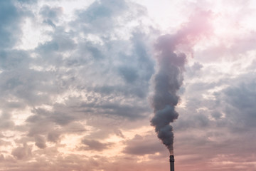 Pipe of a production factory with fumes smoke emission into the atmosphere on the background of blue cloudy skies.