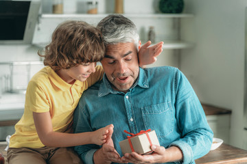 Son making surprise and gives father present box