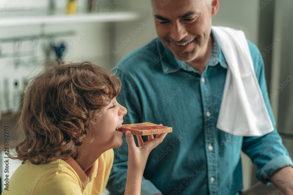 Wall mural Mature father looking at son with toast bread in hands