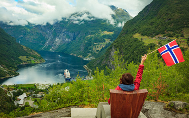 Fototapeta na wymiar Tourist over Geiranger fjord holds norwegian flag