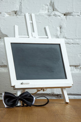 Close-up of a miniature chalk board and bow tie on a white brick wall background, selective focus