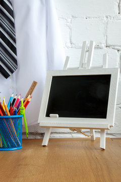 School supplies, miniature chalk board on the table against the background of a white shirt with a tie on a hanger, soft focus