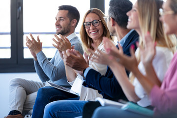 Happy business team clapping after listening the conference while sitting on coworking space.
