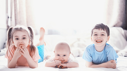 Children lie on the bed next to the newborn baby, little sister.