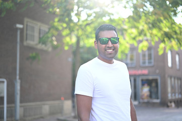 Good looking and happy man wearing sunglasses and walking in the city on a beautiful summer day