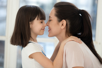 Happy mother and kid daughter touch noses bonding together