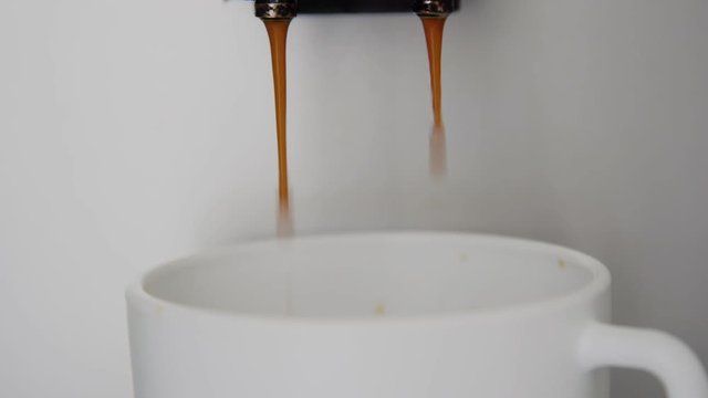 modern coffee machine pours ready hot beverage into white cup through black dispenser extreme close view