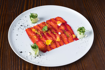 Salmon fish carpaccio on white plate decorate with slices of cucumbers