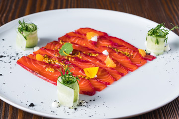 Salmon fish carpaccio on white plate decorate with slices of cucumbers, close up