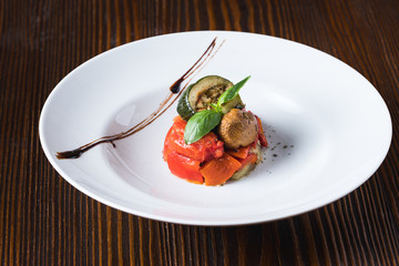 Grilled vegetables, tomatoes, cabbages, zukini and mushroom, decorated with basil on white plate
