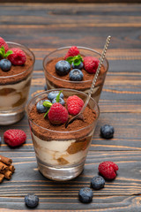 Classic tiramisu dessert with blueberries and strawberries in a glass cup on wooden background