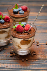 Classic tiramisu dessert with blueberries and strawberries in a glass cup on wooden background