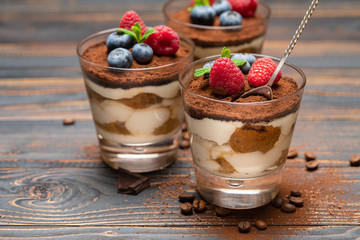 Classic tiramisu dessert with blueberries and strawberries in a glass cup on wooden background
