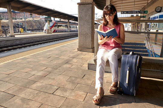 woman reading a book while waiting for the train with a suitcase