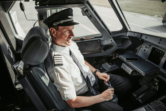 Serious man in uniform looking through window before flight in cockpit