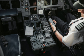 Adult pilot in cockpit looking at screen of his smartphone