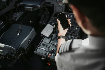 Caucasian pilot in cockpit looking at screen of his smartphone