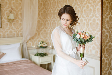 Pretty young Bride.Brown-haired woman with classic wedding hair-style. Boudoir morning of the bride. Taking wedding bouquet in her hands