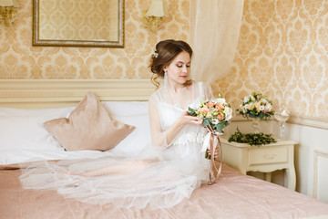 Pretty young Bride.Brown-haired woman with classic wedding hair-style. Boudoir morning of the bride. Taking wedding bouquet in her hands