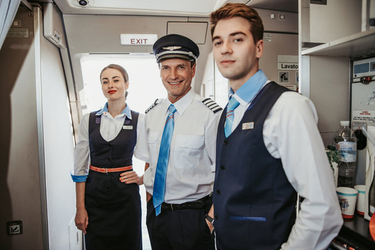 Smiling Caucasian pilot with flight attendants standing on airplane board