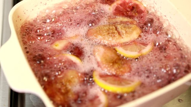 Boiling compote with figs, sliced lemon, red wine and sugar in ceramic pot on burner : ASMR