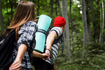 Man and woman with backpack go one after another on hiking trail path in forest woods