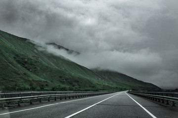 Asphalt road in the mountains on a cloudy gray day. Mountain landscape