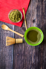 Match green tea in a bowl on a wooden surface with a red napkin. Top view, contains antioxidants, detox. Vertical orientation