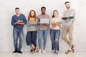 Group of diverse friends posing with gadgets and books